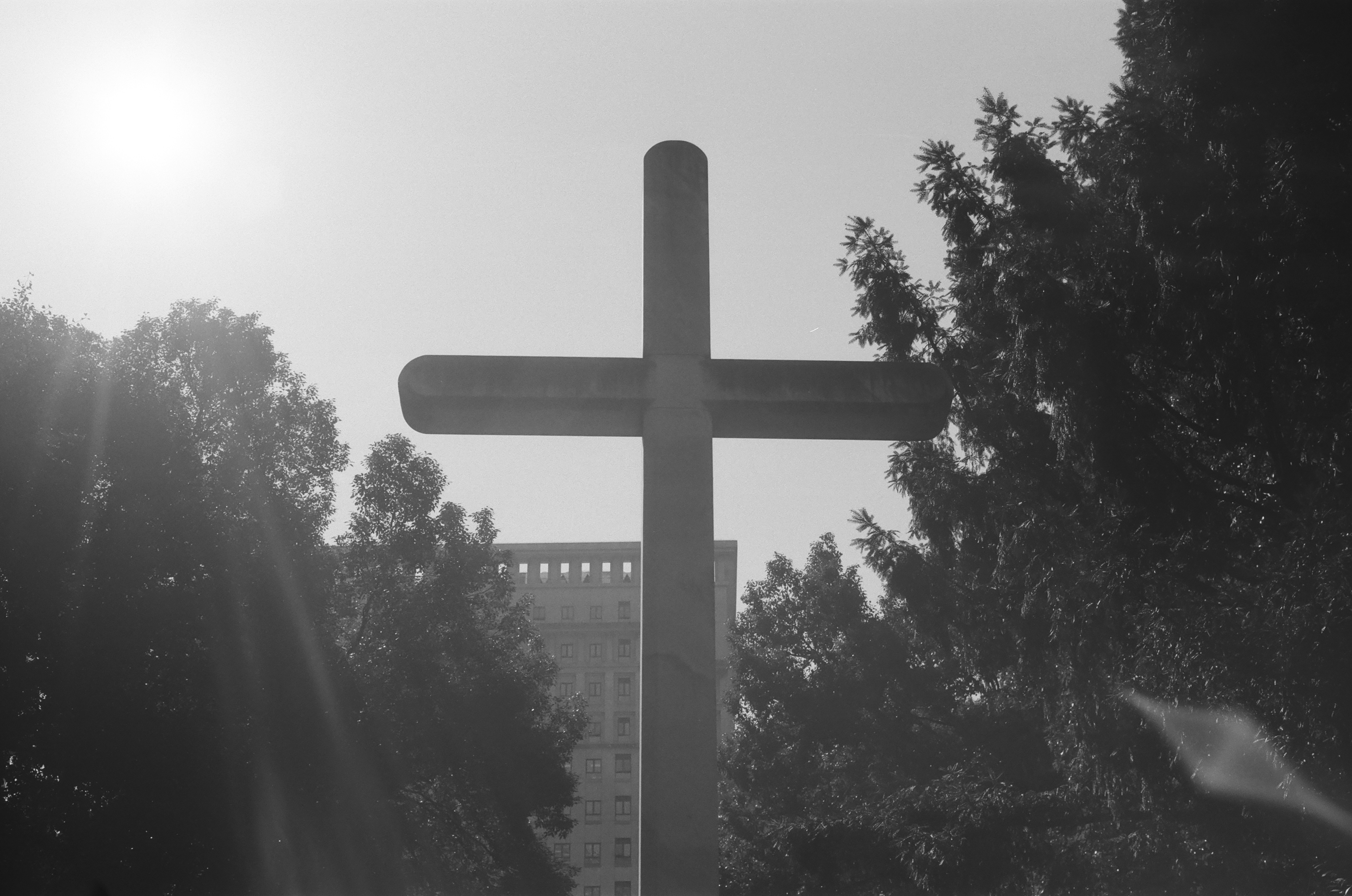 a black and white photo of a cross with trees in the background