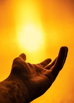 A hand is reaching out towards a bright, golden light. The background is filled with a warm, glowing ambiance, creating a sense of warmth and serenity.