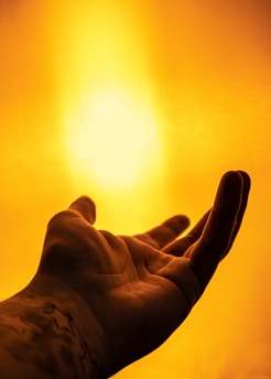 A hand is reaching out towards a bright, golden light. The background is filled with a warm, glowing ambiance, creating a sense of warmth and serenity.