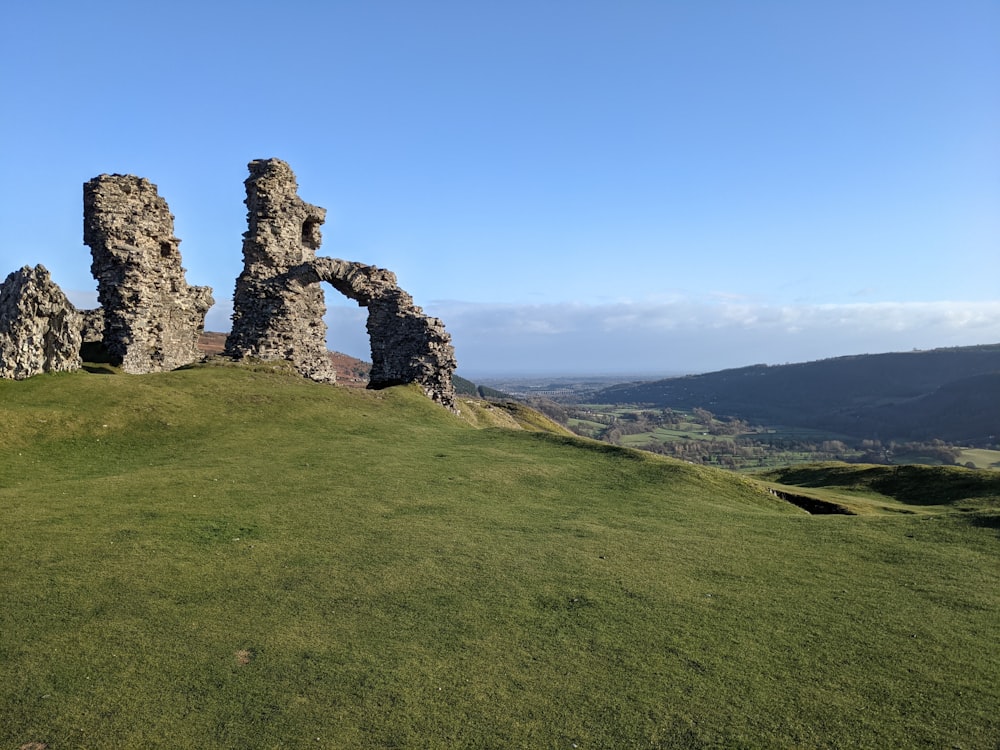 a stone structure on a grassy hill with mountains in the background