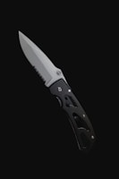 A folding knife with a partially serrated blade and a black handle is set against a stark black background. The handle has cutout designs that contribute to its lightweight appearance.