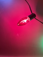A single red bulb lit with a smooth, reflective surface, mounted on a black socket. The light emitted casts a pinkish hue on the surrounding wall.