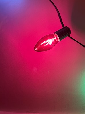 A single red bulb lit with a smooth, reflective surface, mounted on a black socket. The light emitted casts a pinkish hue on the surrounding wall.