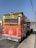A vibrant food truck parked on the side of the road, featuring a bright red color with yellow accents and signs advertising 'Birria de Res' and 'Bone Marrow Tacos.' The truck has a prominent logo with a bull's skull and the name 'Pepe's Red Tacos.' An open serving window is visible on the side.