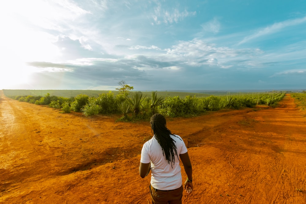 a woman walking down a dirt road in the middle of a field