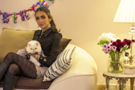 A smiling pet owner holding their cat dressed in a cozy, tailor-made outfit.