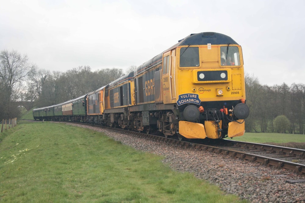 a yellow train traveling down train tracks next to a lush green field