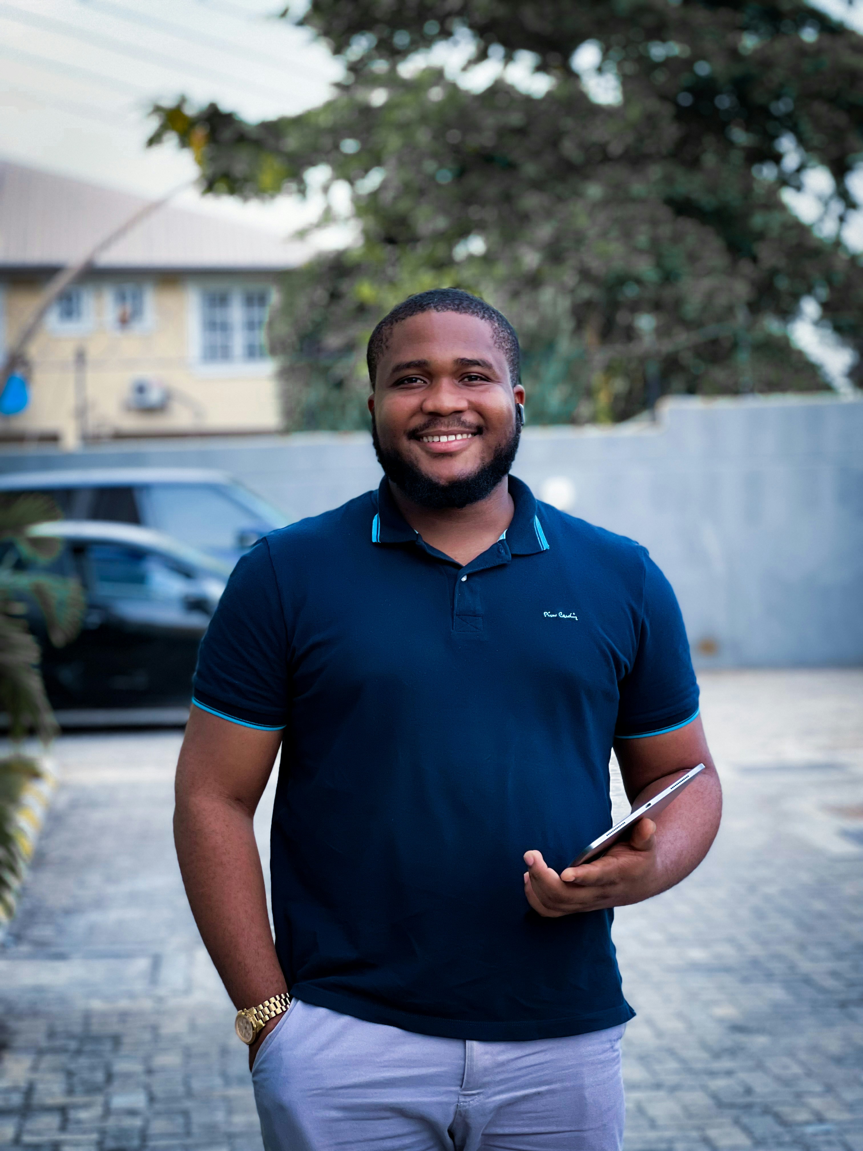 great photo recipe,how to photograph a man standing and smiling with his hand in his pocket outdoor.; a man in a blue shirt is holding a cigarette