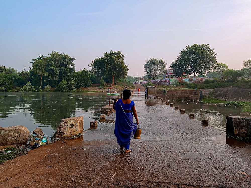 a woman in a blue sari walking along a river