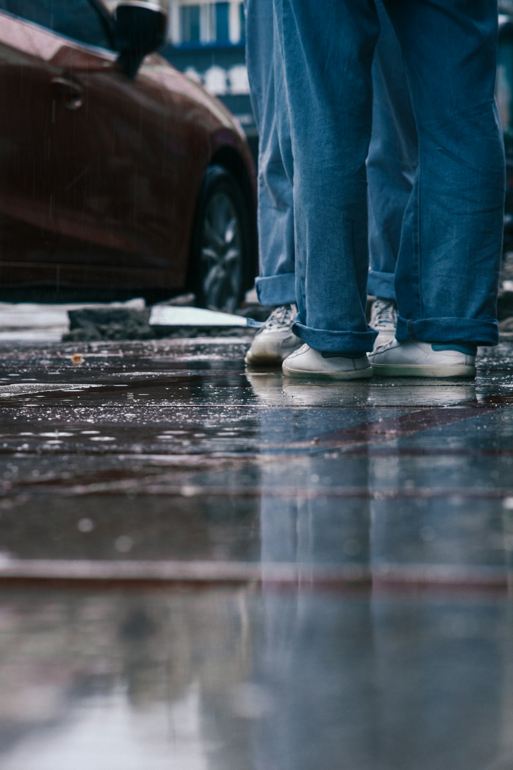 a person standing on a wet sidewalk next to a red car