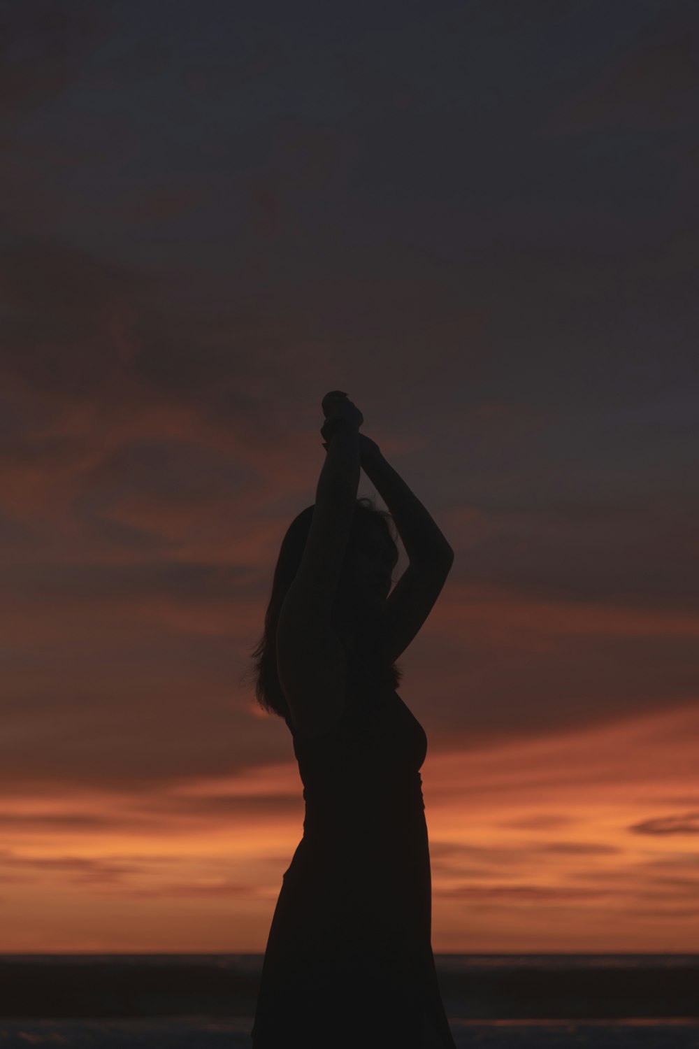 a silhouette of a woman holding a surfboard at sunset