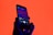 A hand holds a smartphone displaying a music player app with a song titled 'Change' by 'Like Crashing Waves'. The background is a vibrant orange, creating a striking contrast with the phone's dark silhouette and screen.