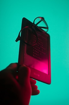 a hand holding a cell phone with a pair of glasses on top of it