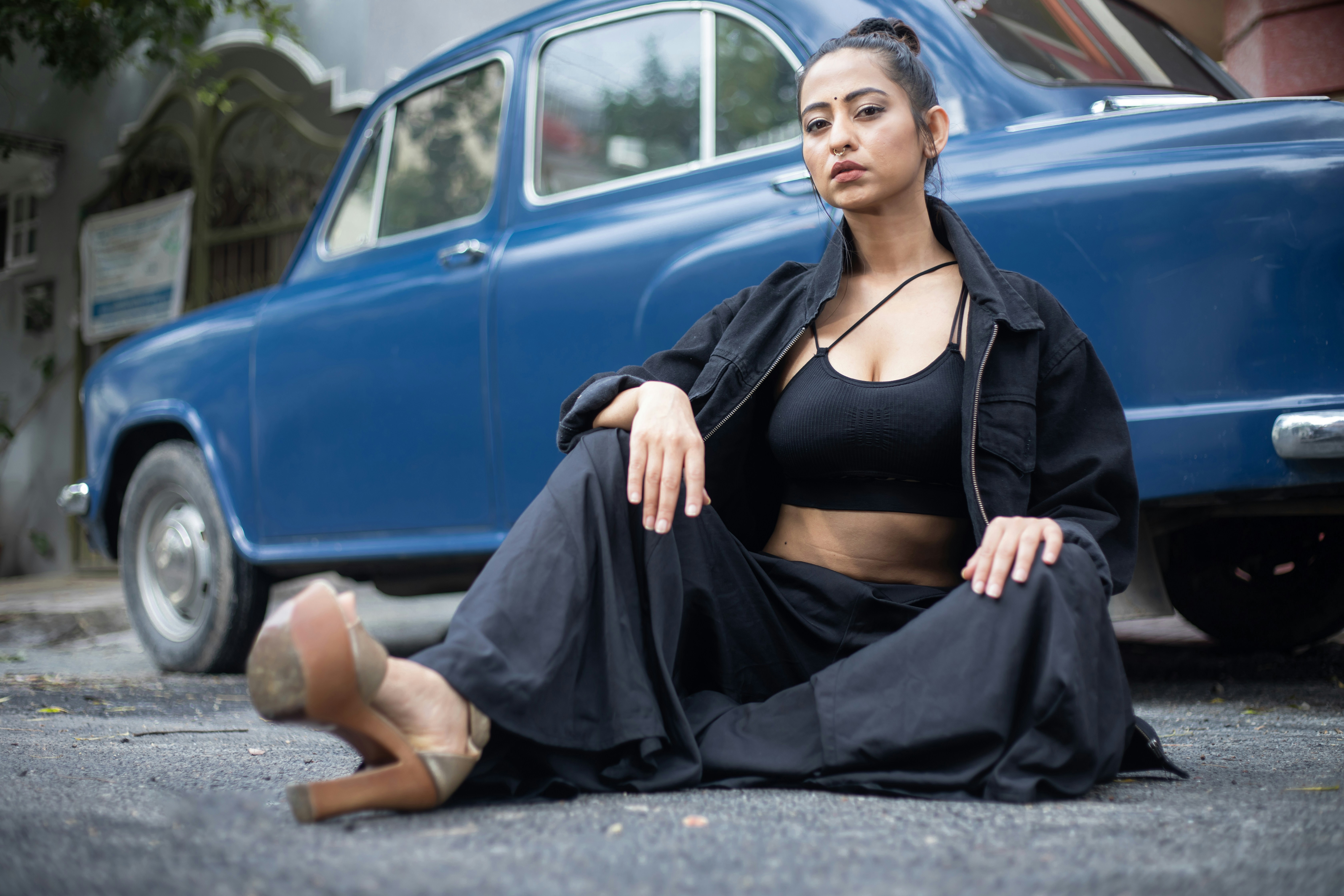 a woman sitting on the ground next to a blue car