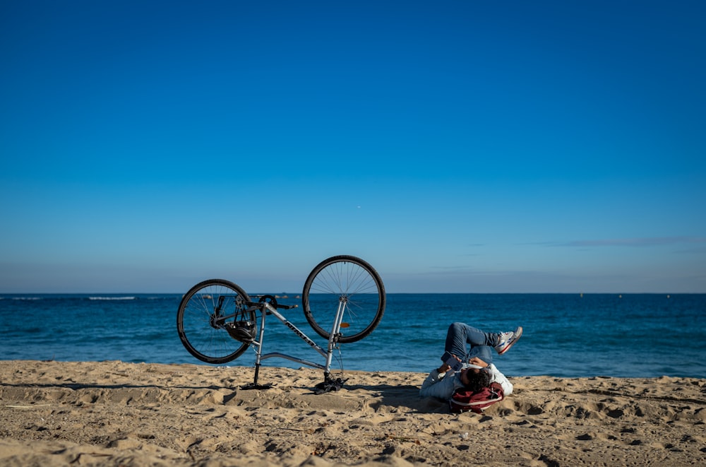 a person laying on the beach next to a bike