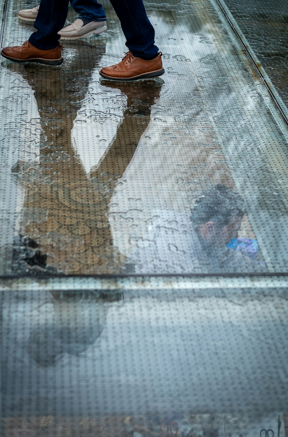 Una persona parada en una pasarela con su reflejo en un charco