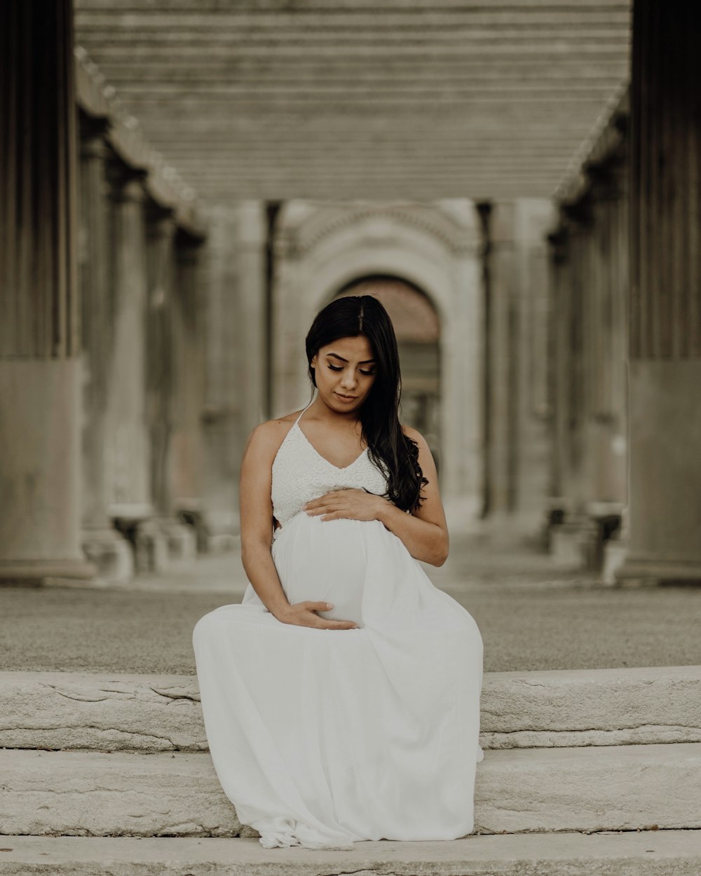a pregnant woman in a white dress sitting on steps