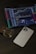 An iPad displays a cryptocurrency trading platform with various charts and numbers. Next to the iPad, there is a white smartphone laid flat on a dark, textured surface. A square glass perfume bottle with some liquid inside is positioned beside the smartphone.