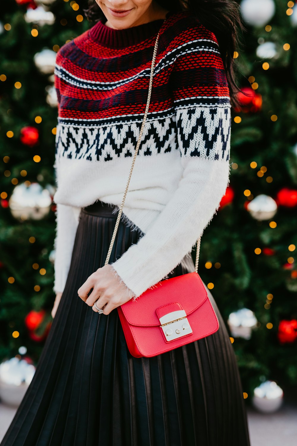 a woman wearing a black pleated skirt, a white sweater, and a red