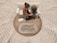 A small figurine display shows two figures sitting on a sofa on a wooden base with intricate lace around it. One figure places a comforting hand on the other’s arm, symbolizing support and togetherness. A plaque with an inspirational quote about encouragement and prayer is visible.