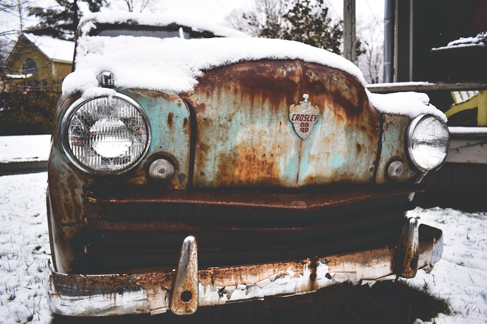 an old rusty car with snow on the hood