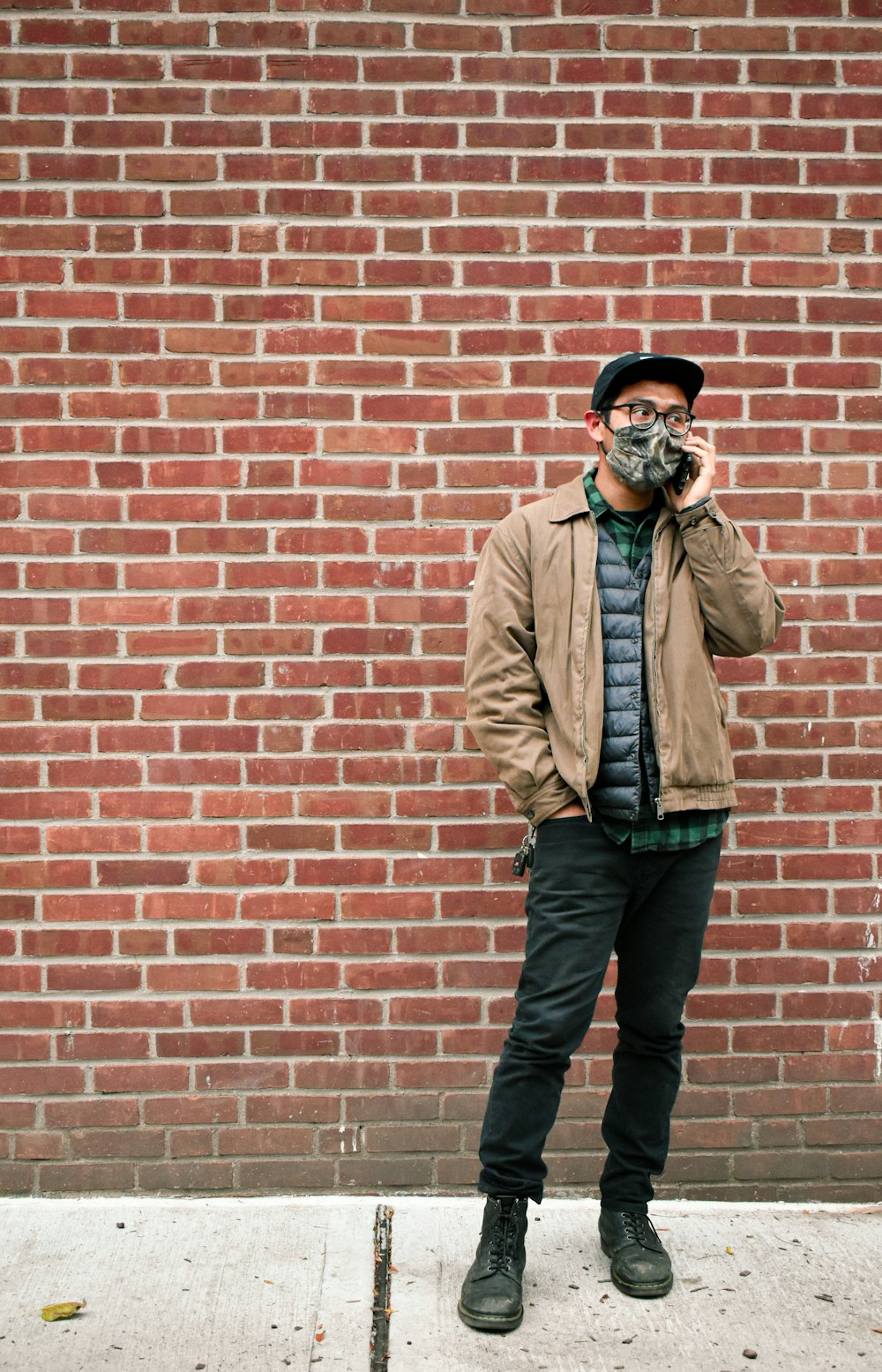 a man standing in front of a brick wall talking on a cell phone