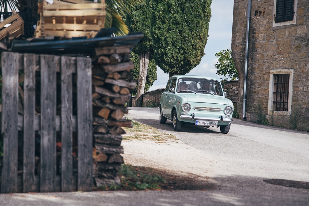 a small car driving down a street next to a wooden fence