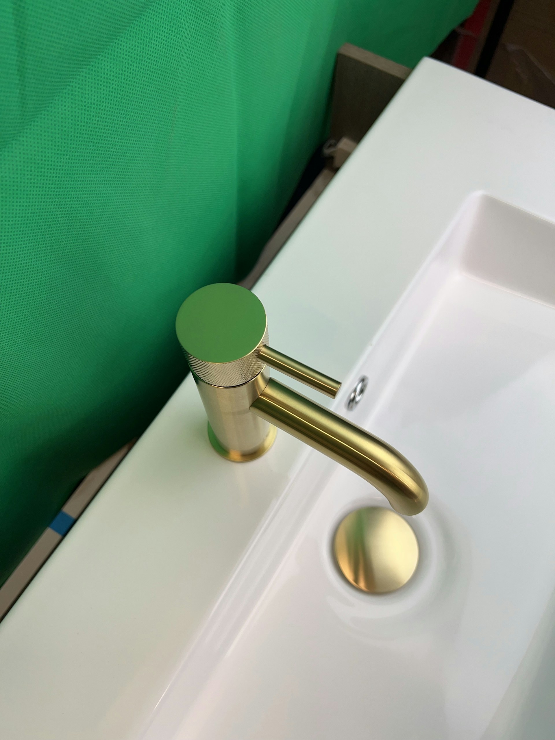 a bathroom sink with a gold faucet and a green curtain