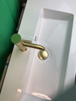 A modern white ceramic washbasin with smooth curves, paired with a gold-accented faucet.