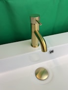 a bathroom sink with a gold faucet and a green background