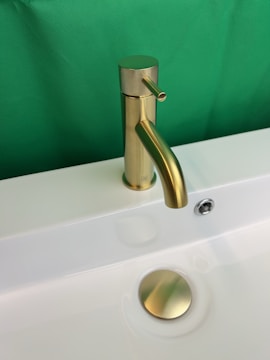 a bathroom sink with a gold faucet and a green background