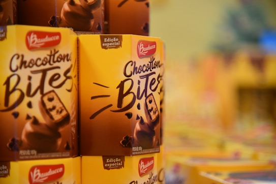 Several boxes of Bauducco Chocottone Bites with a bright yellow and brown design are displayed. The packaging features an image of the chocolate chip panettone bites and branding information.