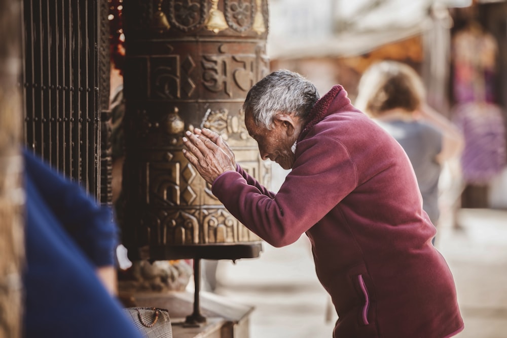 a man in a red sweater is praying in front of a bell