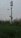 A tall, metal structure equipped with multiple security or surveillance cameras is standing in a field of tall grass and plants. The sky is overcast with scattered pinkish clouds, suggesting an early morning or evening setting.