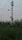 A tall, metal structure equipped with multiple security or surveillance cameras is standing in a field of tall grass and plants. The sky is overcast with scattered pinkish clouds, suggesting an early morning or evening setting.