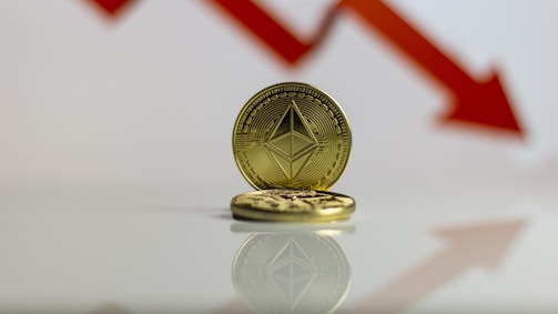 A gold-colored coin with Ethereum's symbol is prominently displayed against a backdrop of a red downward arrow, symbolizing a decrease or decline.