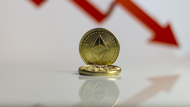 A gold-colored coin with Ethereum's symbol is prominently displayed against a backdrop of a red downward arrow, symbolizing a decrease or decline.