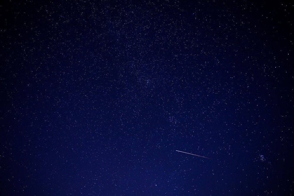 a night sky with stars and a plane in the distance