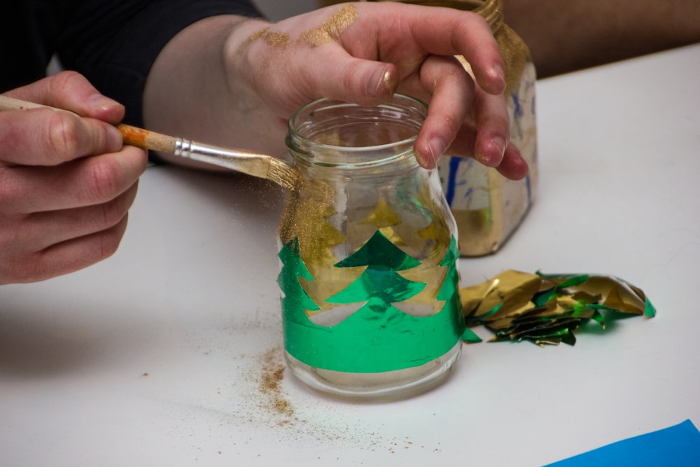 a person is painting a jar with green and gold paint