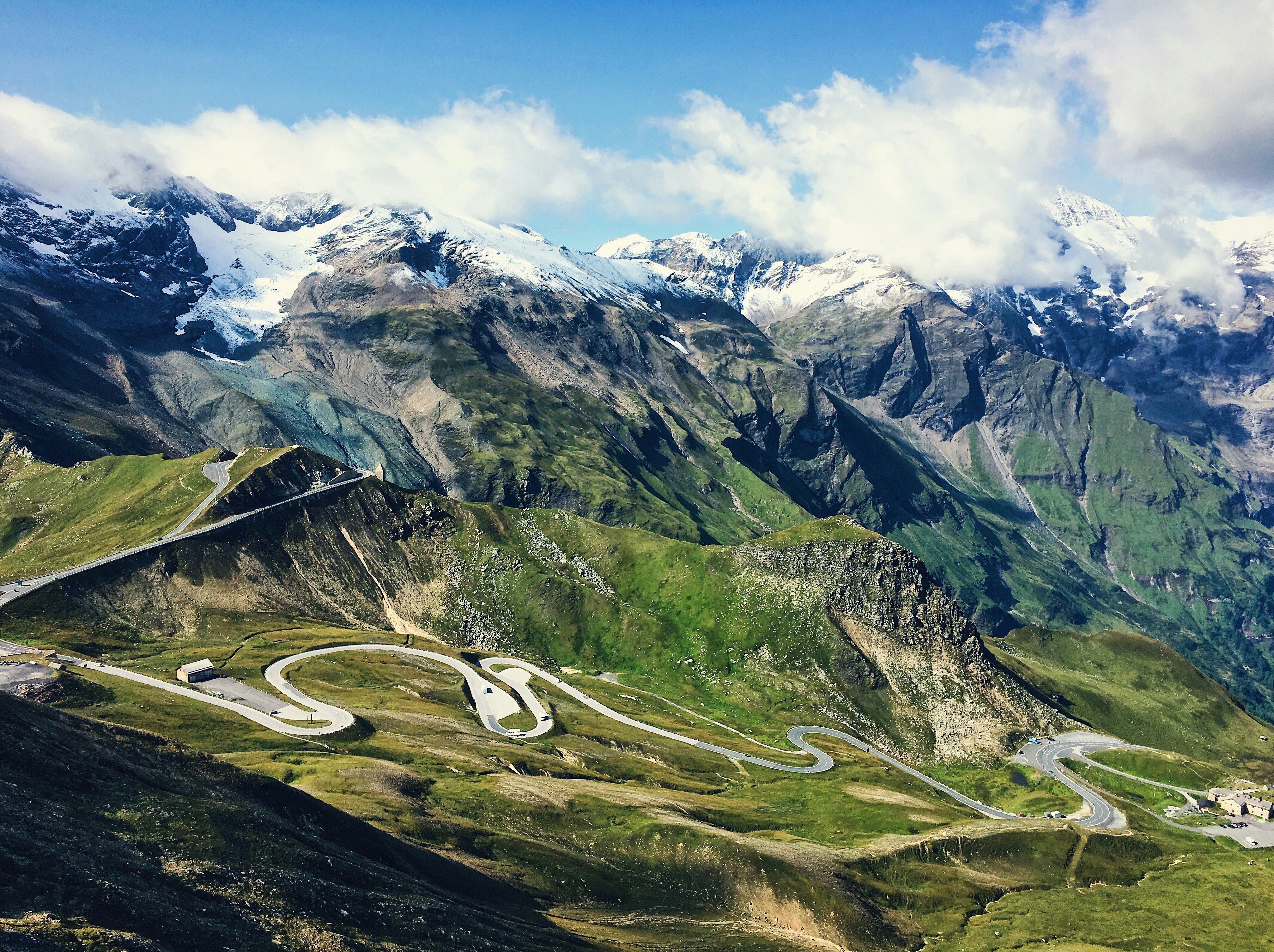 a winding road in the mountains with snow capped mountains in the background