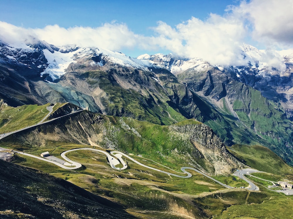 a winding road in the mountains with snow capped mountains in the background