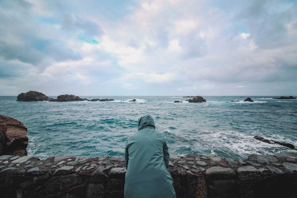 a person sitting on a wall looking out at the ocean