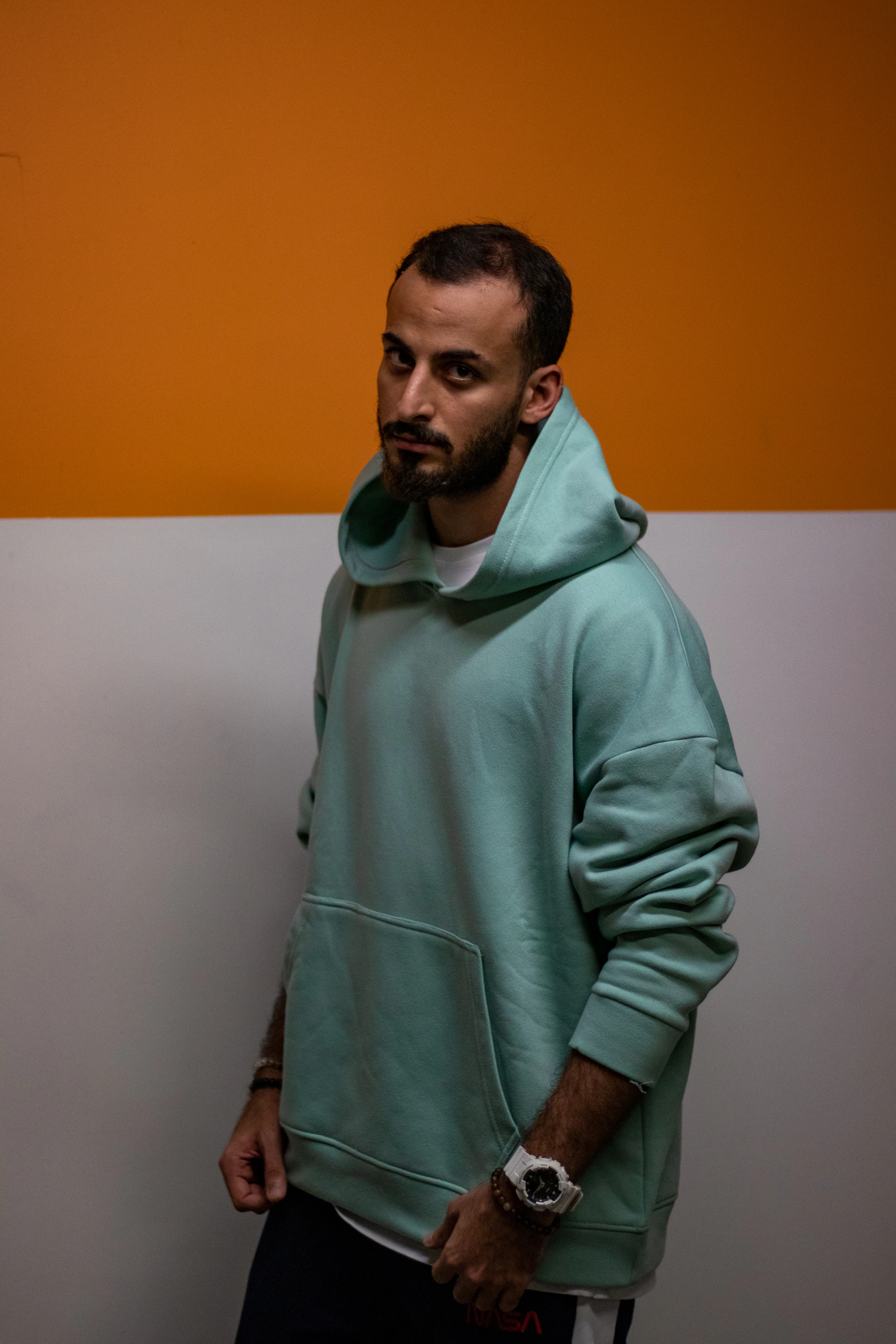 Man in a mint green oversized hoodie against an ochre wall