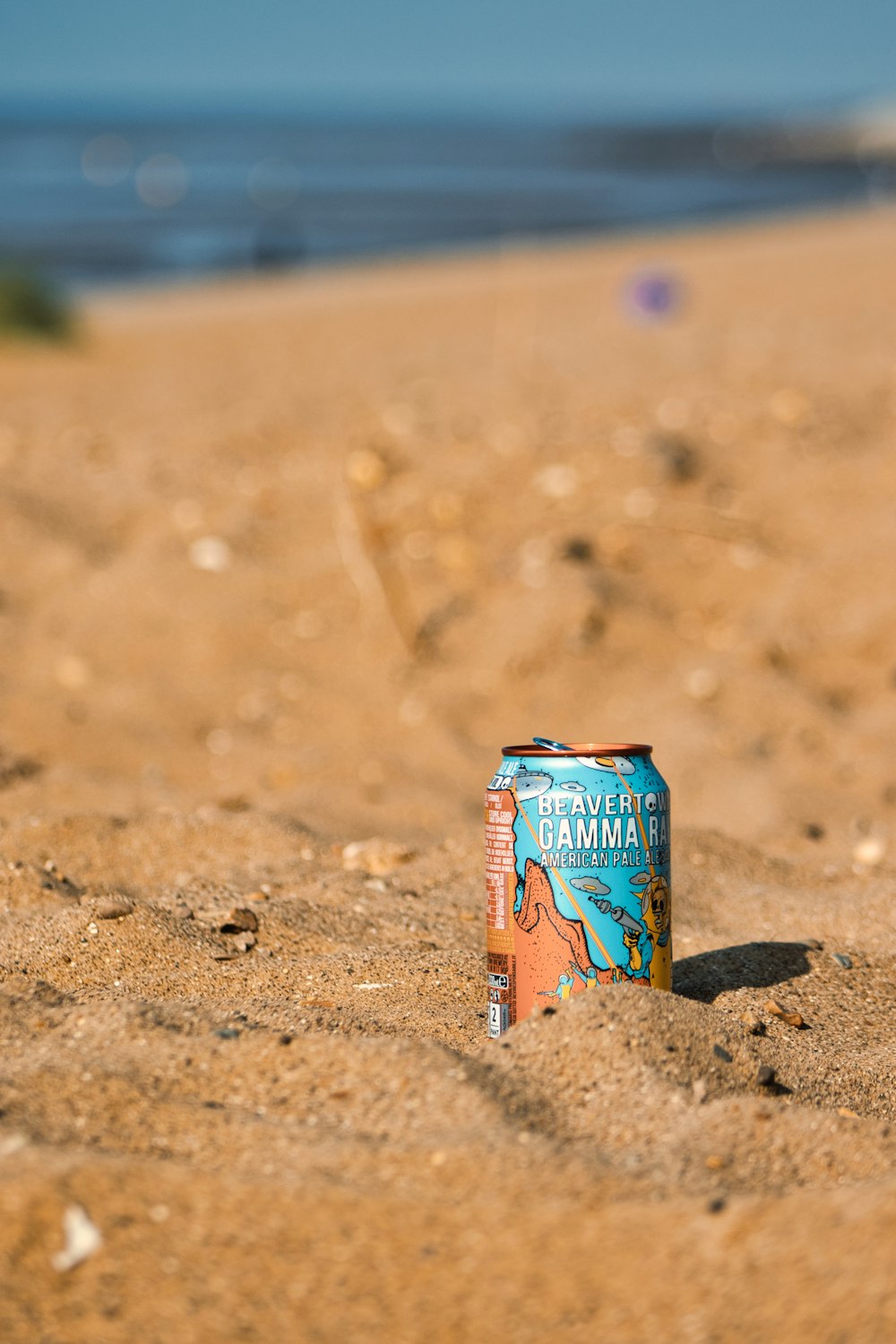 a can of beer sitting on top of a sandy beach