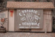 A small wooden structure with a shingled roof displays a large banner advertising psychic readings with elements like a hand, moons, and stars. To the left, a sign denotes reserved parking for a 'mystical journey' alongside a potted plant with orange flowers and a red bow on the wall.