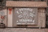 A small wooden structure with a shingled roof displays a large banner advertising psychic readings with elements like a hand, moons, and stars. To the left, a sign denotes reserved parking for a 'mystical journey' alongside a potted plant with orange flowers and a red bow on the wall.