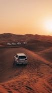 a white car driving through the desert at sunset