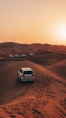 a white car driving through the desert at sunset