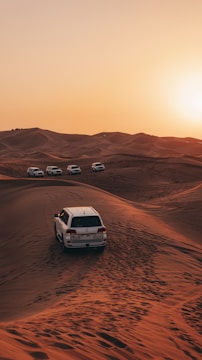 a white car driving through the desert at sunset