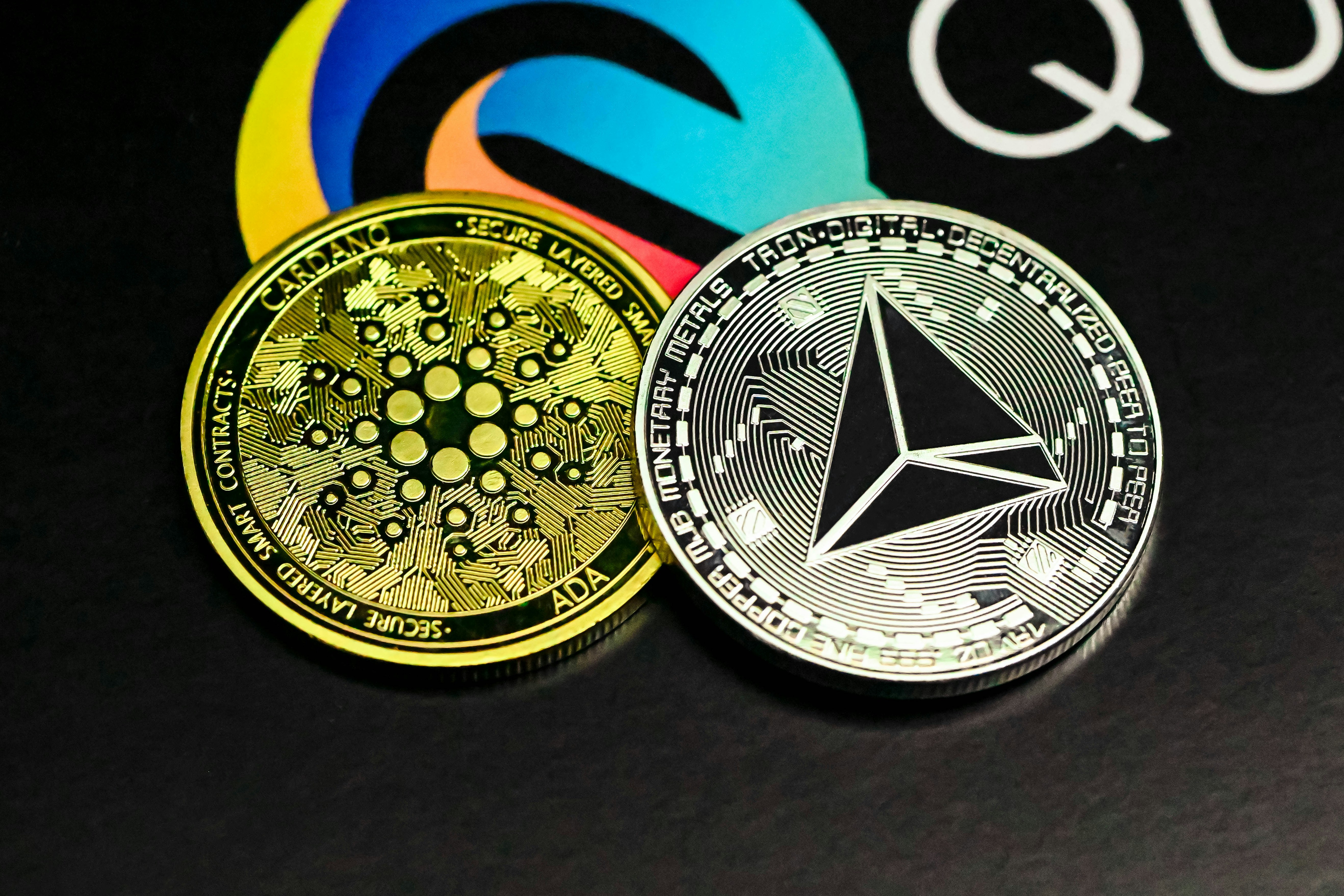 a close up of two different colored coins, TRON and Cardano coins on the Quantitatives logo